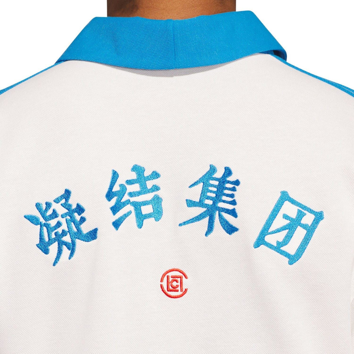 Back of white polo shirt showing blue graphic text and small red emblem near collar.