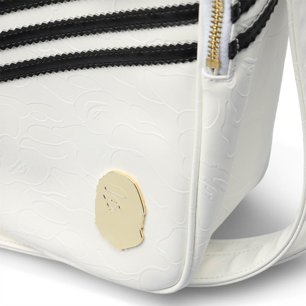 White adidas Originals BAPE bag close-up with gold emblem patch and black zipper stripe