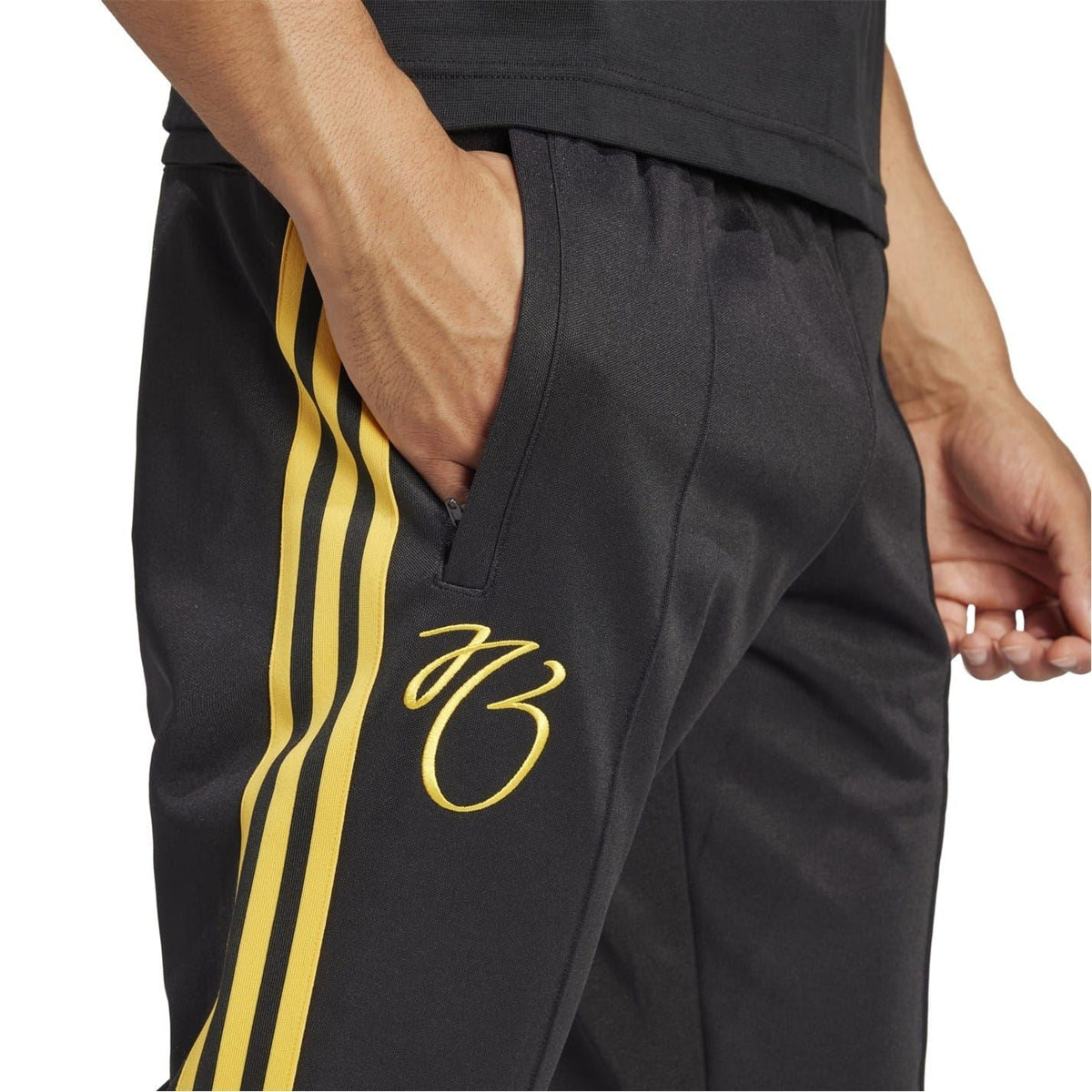 Black track pants close-up with yellow side stripes, “83” script, and front pocket seam