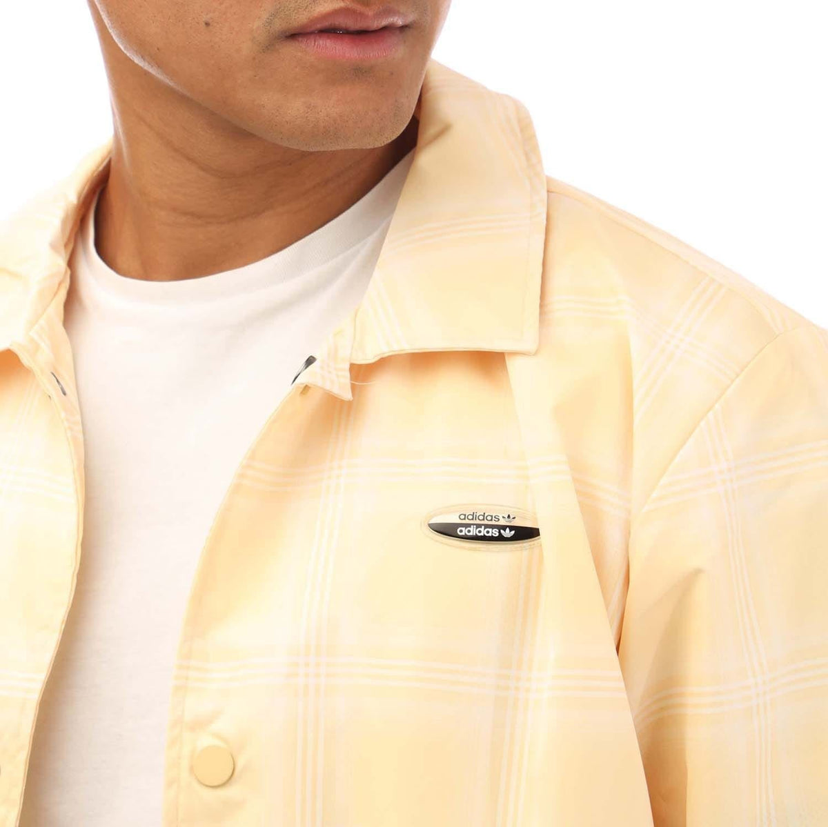 Coach jacket close-up with adidas patch and subtle plaid texture in light yellow