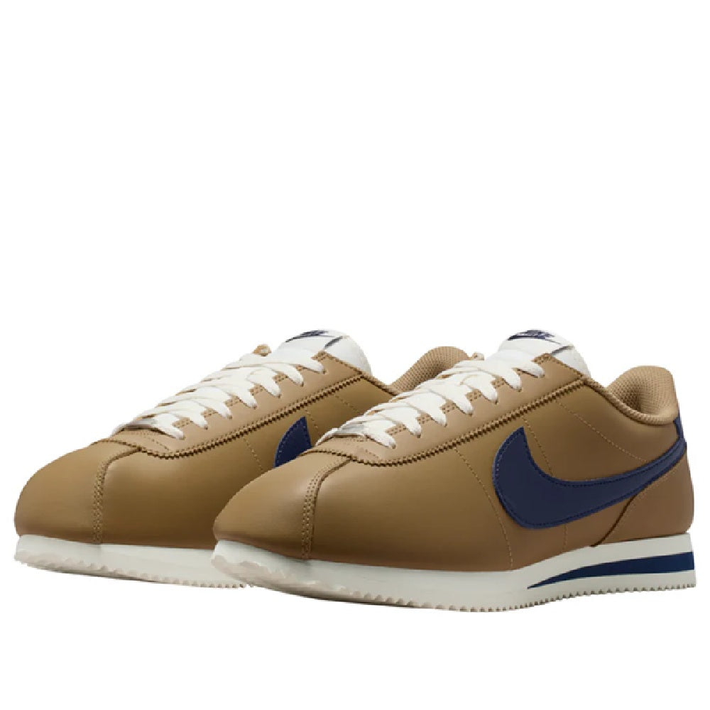 Pair of low-top sneakers in tan with navy swooshes, white laces, and white rubber sole