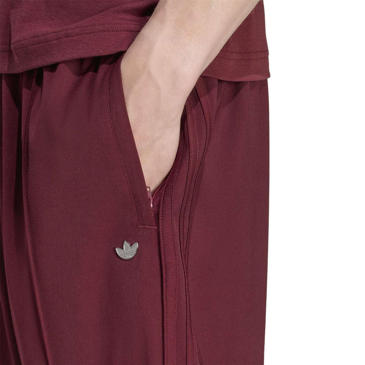 Close-up of maroon drawstring track pants with adidas trefoil patch on pocket