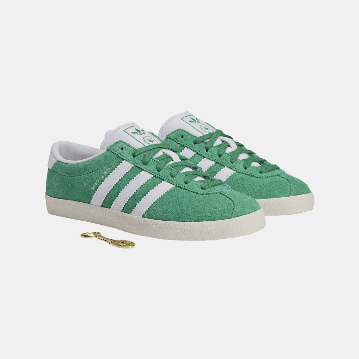 Green suede trainers with white triple stripes and lace-up closure; hang tag included.