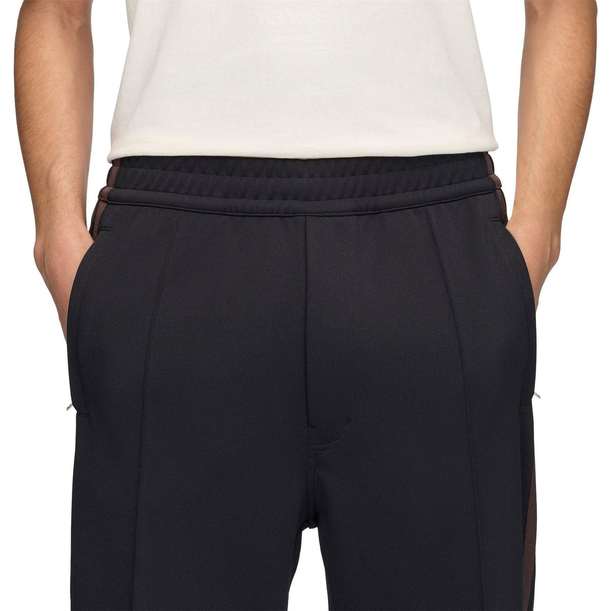 Black track pants with elastic waistband, front seam, and side stripe panels