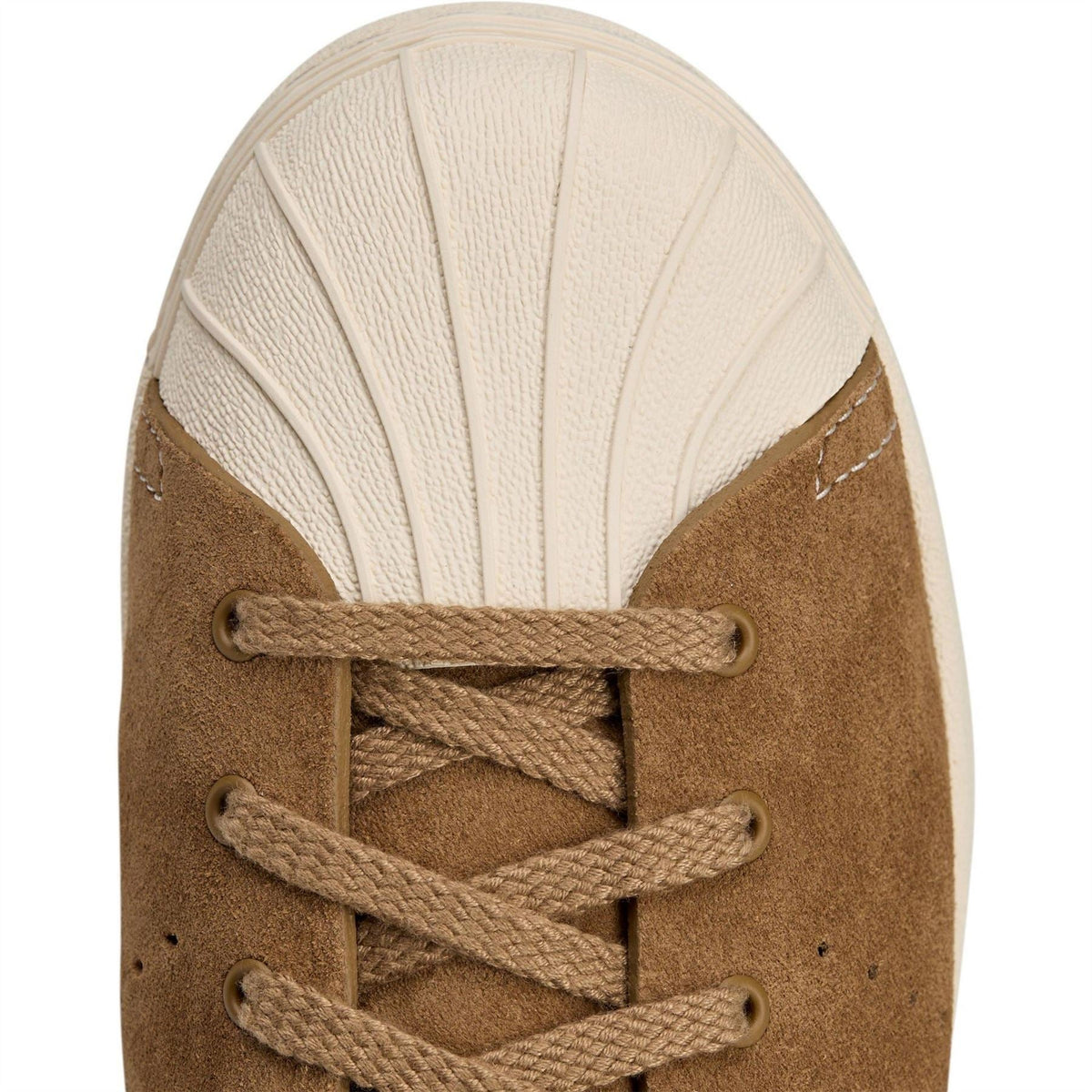 Brown suede tongue with lace-up eyelets and cream rubber cap, close-up