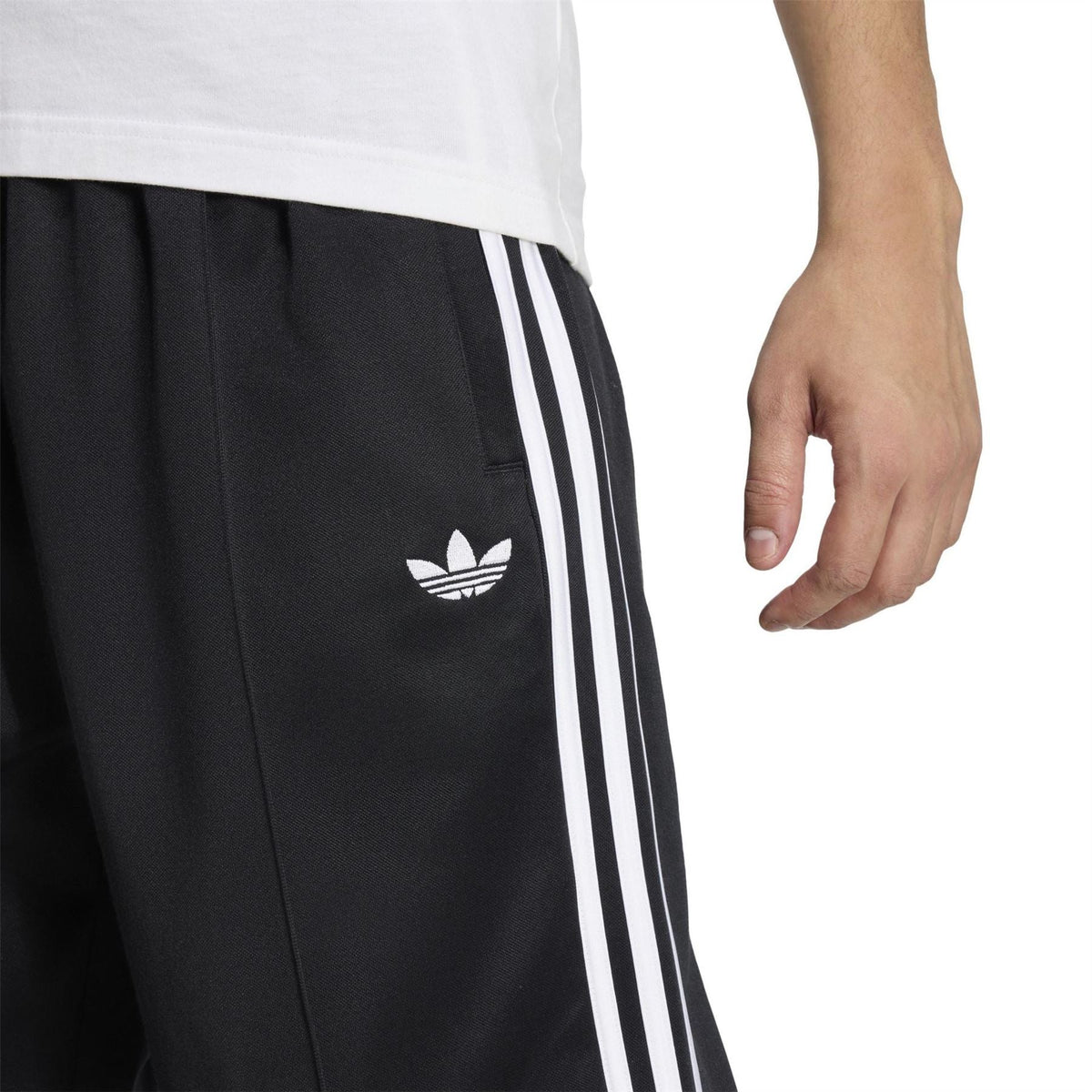 Black track pants detail: adidas trefoil logo and white triple stripe panel on side