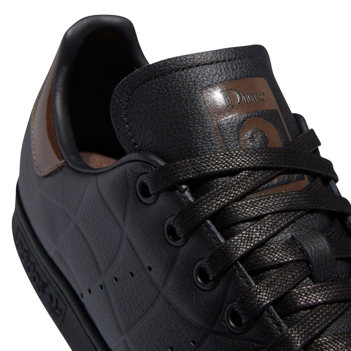 Black leather lace-up trainer close-up with Dime badge and brown collar stitching