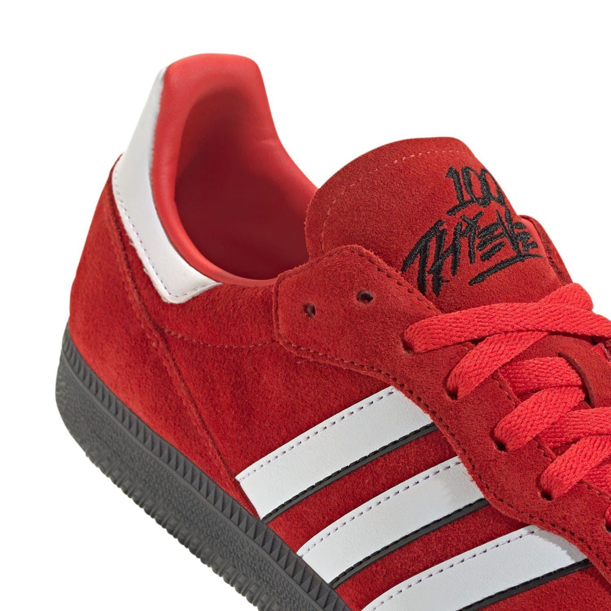Red suede trainer upper detail with white stripes, red laces, and logo print
