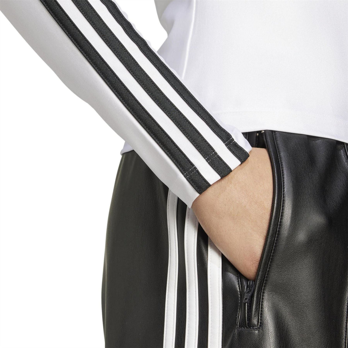 White T-shirt sleeve with black-and-white three stripes; hand near jacket zip
