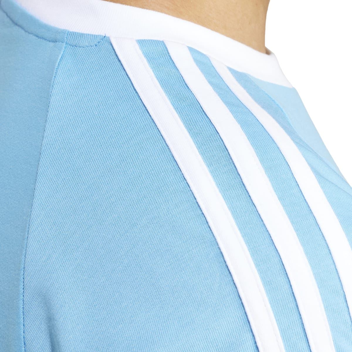 Light blue T-shirt shoulder detail with white three-stripe panel and stitched seam
