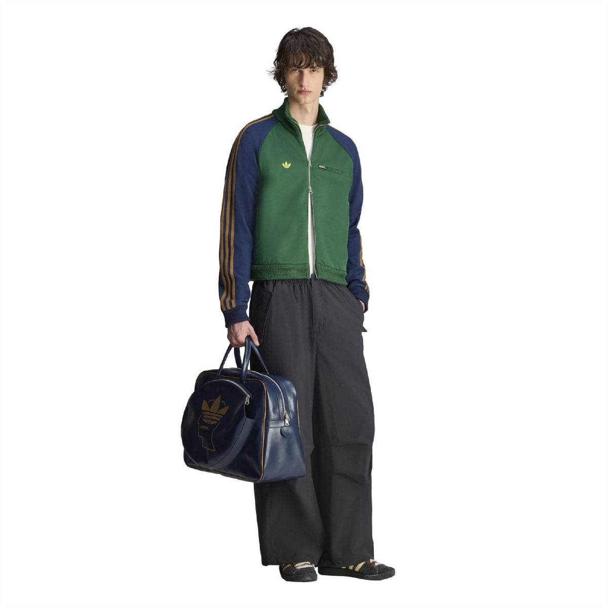 Green track jacket with gold stripe sleeves, full zipper, worn with a navy duffel bag
