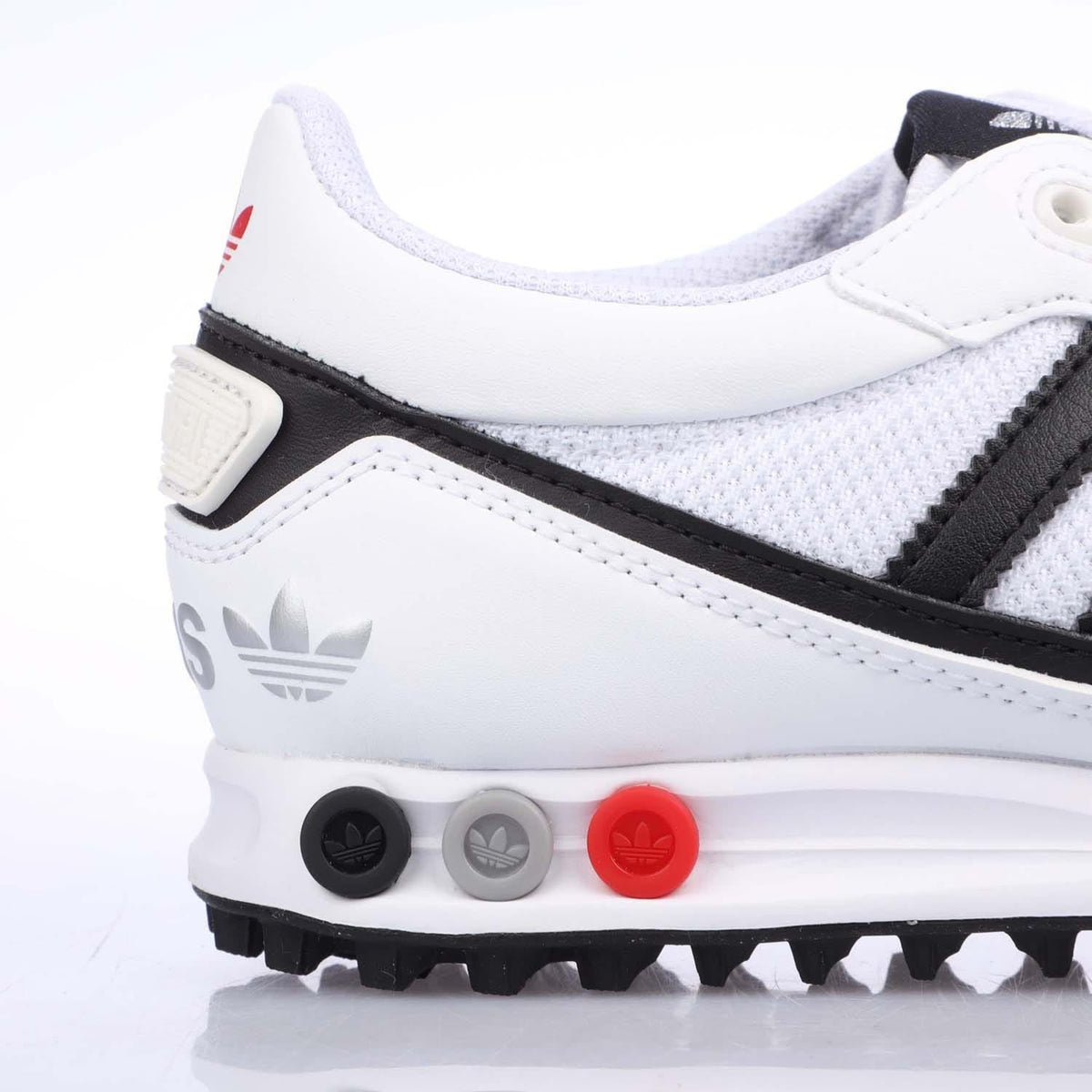 White junior Adidas sneakers with black stripe, mesh upper, and red midsole pod.
