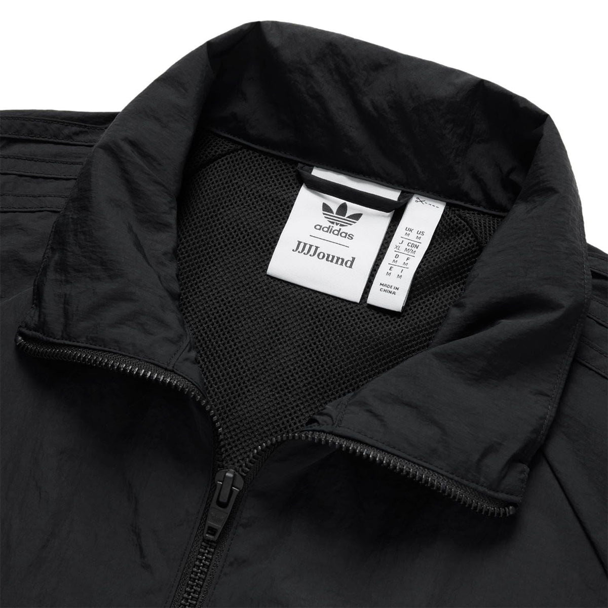 Black track jacket neckline with adidas trefoil and JJJJound label inside collar