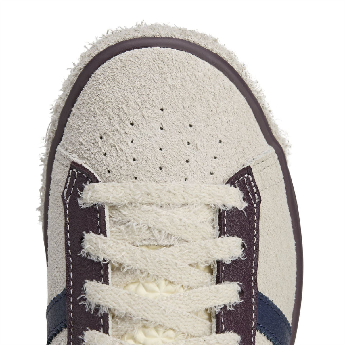 Close-up of white suede toe with perforations and dark lace overlay stitching
