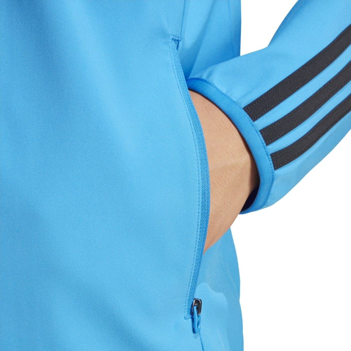 Blue jacket sleeve close-up with black triple stripe and zip pocket detail