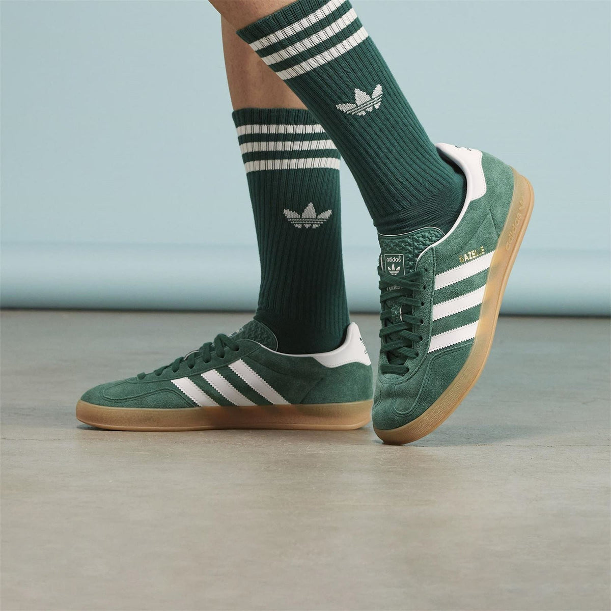 Green adidas Gazelle sneakers with white stripes, worn with dark green socks