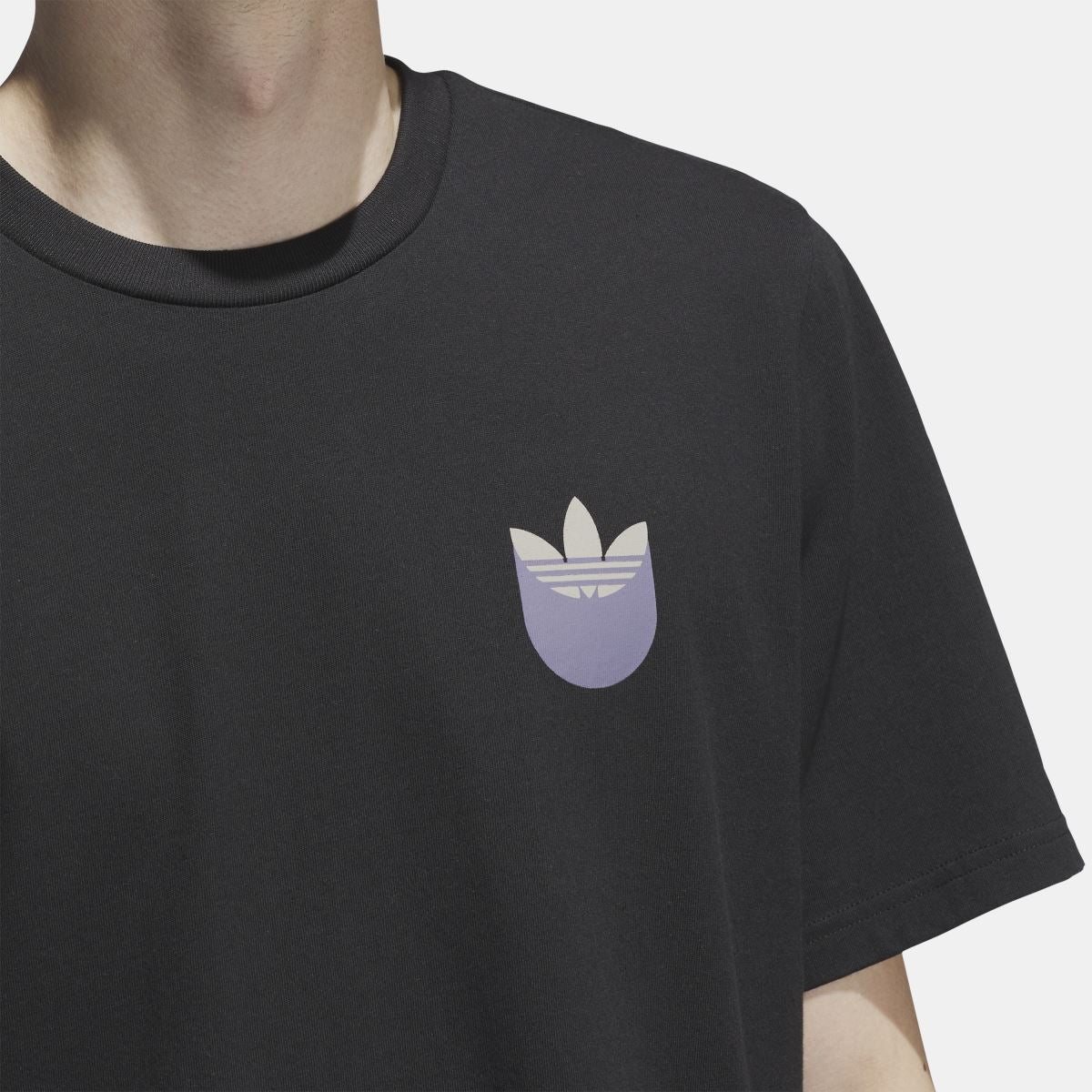 Black t-shirt close-up: small trefoil shadow logo at chest