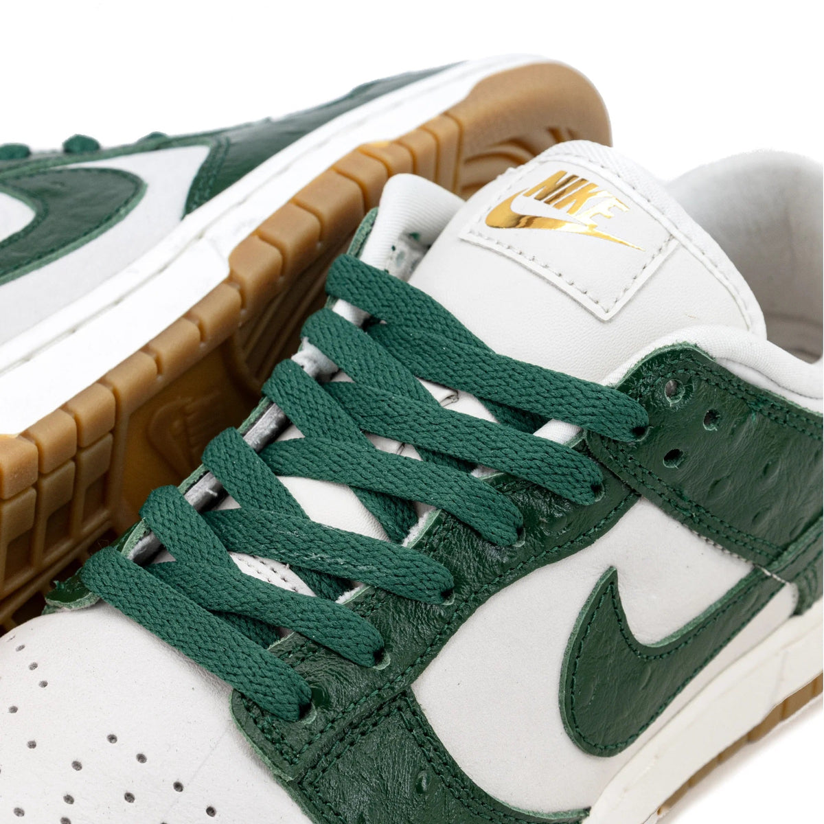 Women's low-top sneaker close-up, green laces over white leather with gold tongue tag.