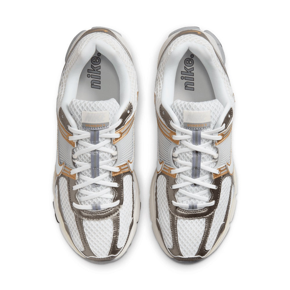 Close-up of white sneaker tongues and toe boxes with gold stripe accents and laces