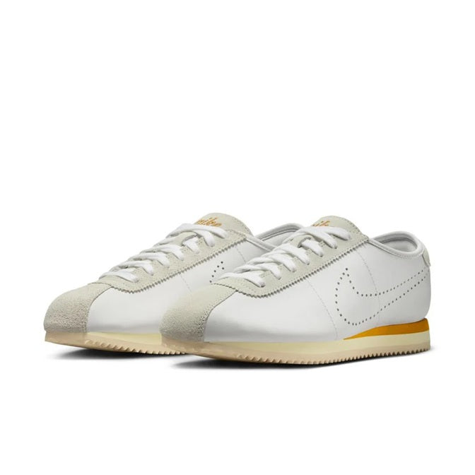 Pair of low-top sneakers with lace-up front, white leather, and bronze accents on side